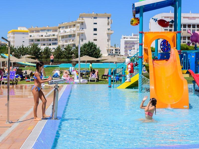 Kinderen spelen in het zwembad met kleurrijke glijbanen in een zonnige hotel tuin.