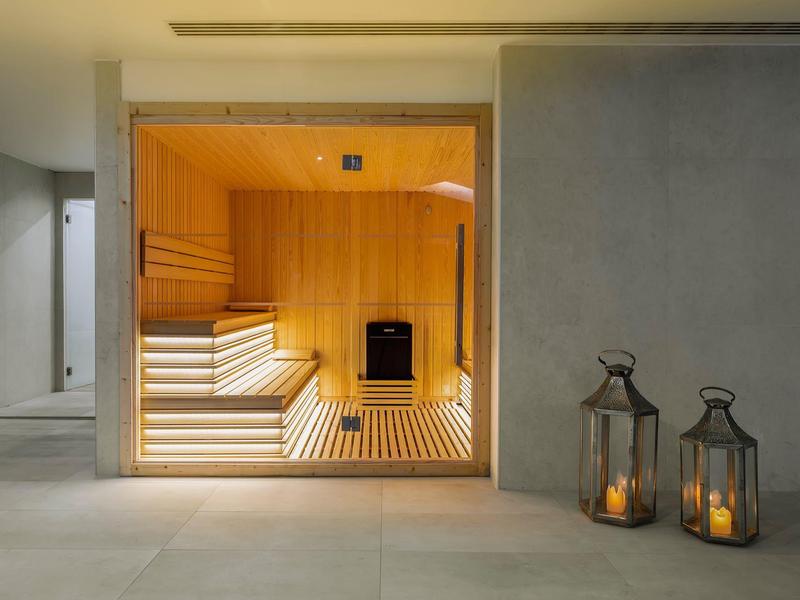 Moderne sauna met houten interieur en twee lantaarns op de vloer voor de deur.