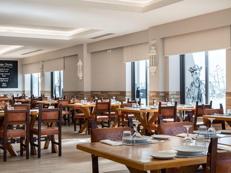 Licht, modern restaurant met houten tafels en stoelen, gedekt met borden en glazen.