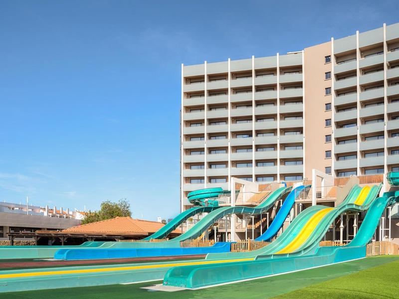 Grote glijbanen voor een hoog hotelgebouw onder een blauwe lucht.