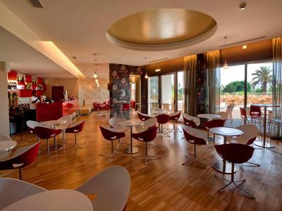 Modern ingerichte ontbijtruimte met ronde tafels en stoelen, groot raam met uitzicht op palmbomen.