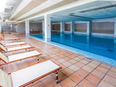 Overdekt zwembad met ligstoelen en terracotta vloer in een hotel.