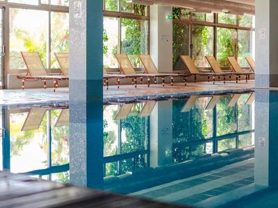 Overdekt zwembad met ligstoelen en grote ramen die daglicht binnenlaten.