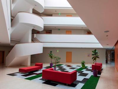 Lichte hotellobby met rode zachte banken en moderne wenteltrap.