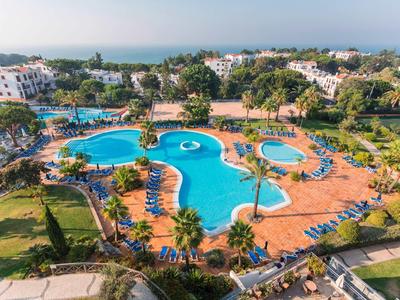 Groot hotelzwembad met parasols omringd door tropisch groen bij heldere lucht.
