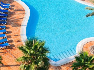 Aantrekkelijk zwembad met blauwe ligstoelen en palmbomen op een terras.