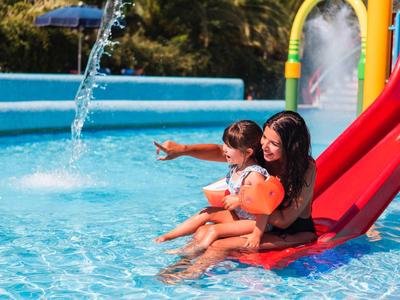 Moeder en kind glijden samen van een rode glijbaan het zwembad in.