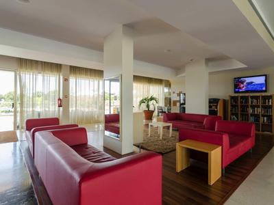 Moderne hotel-lounge met rode banken, houten vloer en grote ramen met uitzicht.