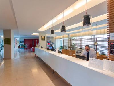 Moderne hotel lobby receptie met lange witte balie en medewerker achter computer.