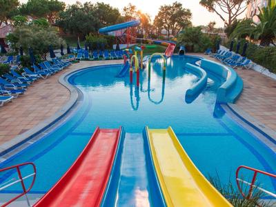 Kleurrijk zwembad met glijbanen bij een hotel met ligstoelen en groen.