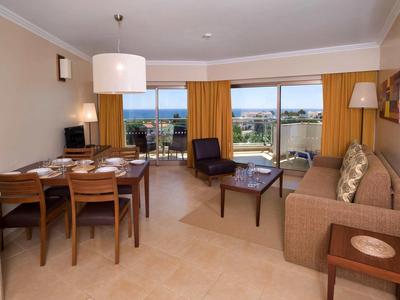 Woon- en eetgedeelte met bruine bank, stoelen, eettafel en uitzicht op balkon en zee.