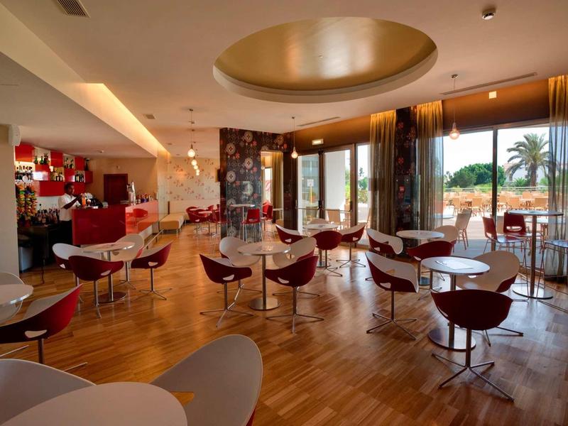 Modern ingerichte ontbijtruimte met ronde tafels en stoelen, groot raam met uitzicht op palmbomen.