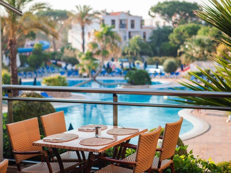 Gezellige tafel met stoelen op terras met uitzicht op zwembad en palmbomen in hotel.