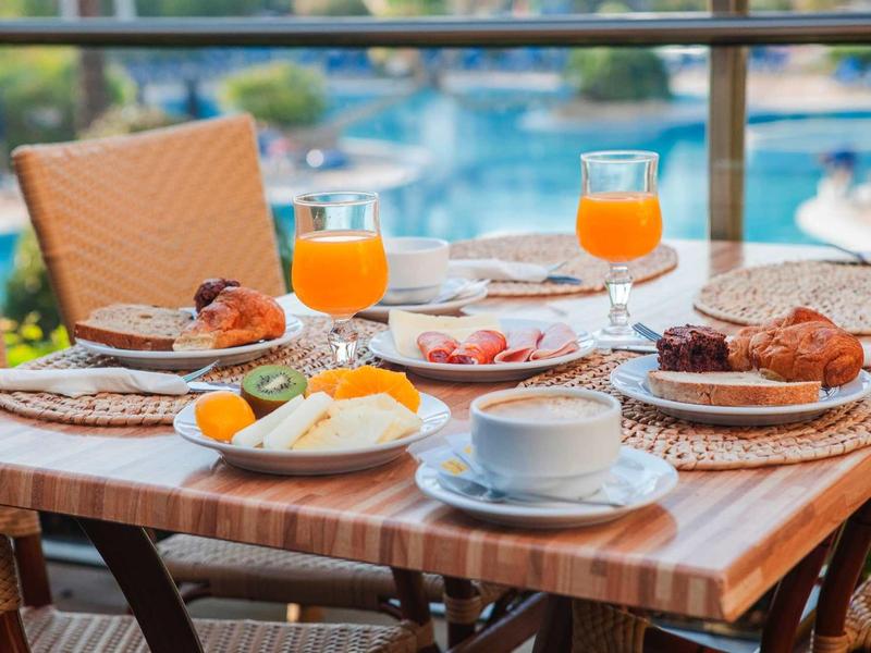 Ontbijttafel met sinaasappelsap, koffie, broodjes en eieren op een balkon met uitzicht op het zwembad.