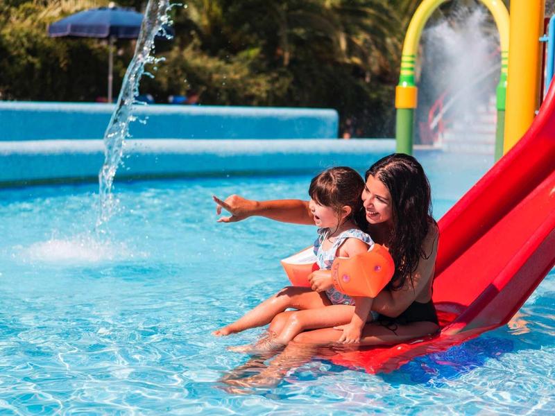 Moeder en kind glijden samen van een rode glijbaan het zwembad in.