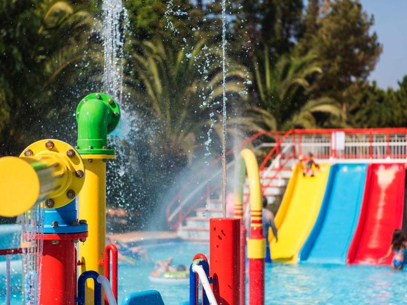 Kleurrijke waterspelen en glijbanen in een zwembadgebied met palmbomen op een zonnige dag.