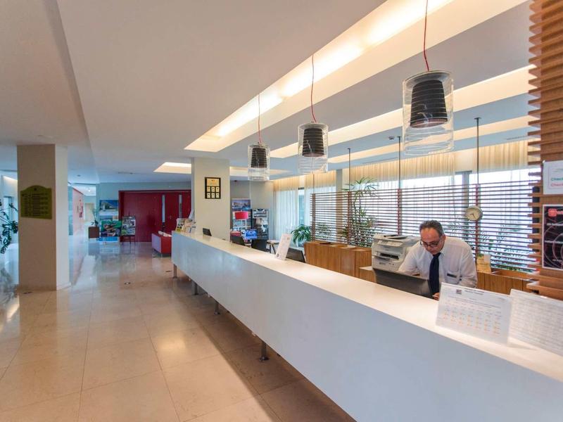 Moderne hotel lobby receptie met lange witte balie en medewerker achter computer.