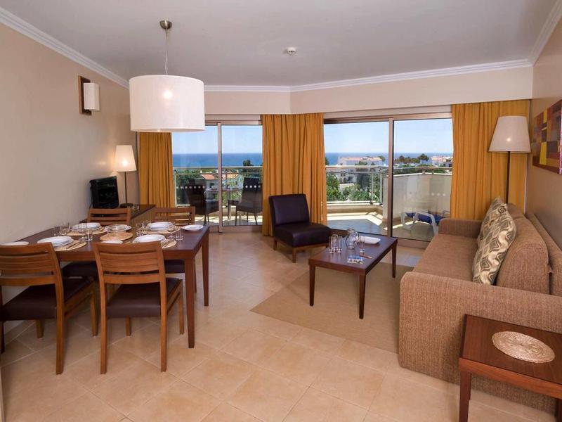 Woon- en eetgedeelte met bruine bank, stoelen, eettafel en uitzicht op balkon en zee.