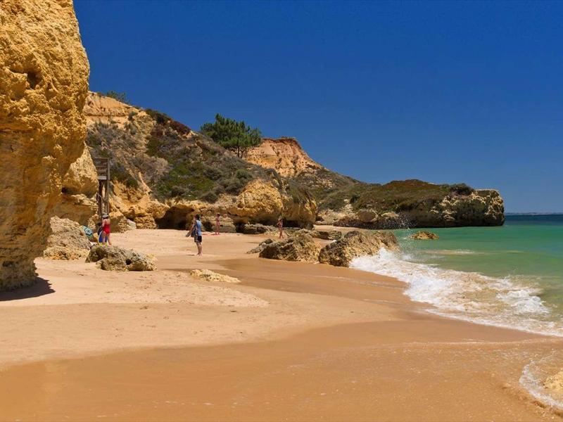 Zandstrand met helder water, kliffen en blauwe lucht langs de kust.