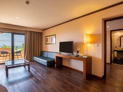 Modern eingerichtetes Hotelzimmer mit Wohnzimmer, TV, Sofa und Terrasse mit Meerblick.