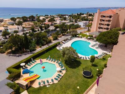 Poolanlage mit zwei Pools, Liegestühlen und Blick auf das Meer in einer Hotelanlage.