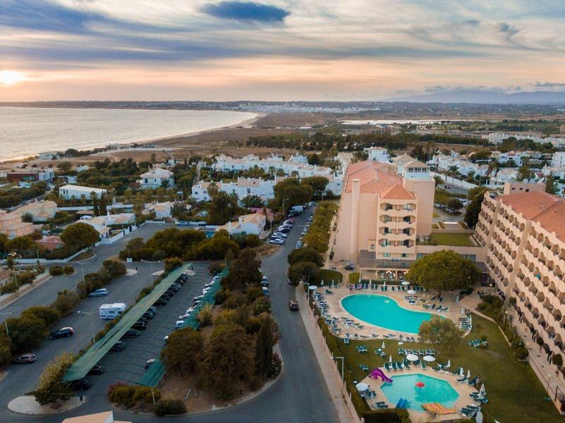 Blick auf Küstenstadt mit Hotels, Pools, Straßen und Meer im Sonnenuntergang.