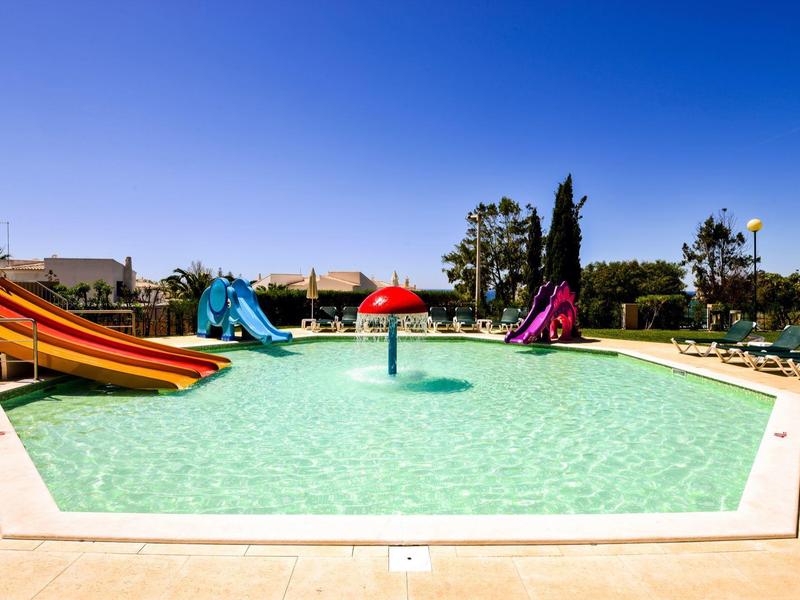 Großer Außenpool mit Wasserrutschen und Sonnenschirmen unter klarem blauem Himmel.