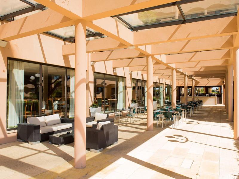 Überdachte Terrasse mit moderner Sitzgarnitur, Holzbalken und großen Schaufenstern im Sonnenlicht.