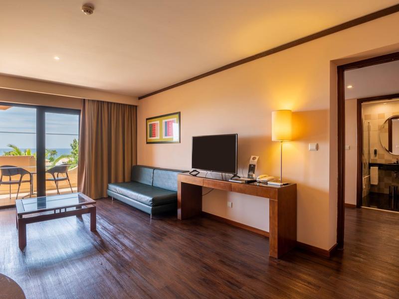 Modern eingerichtetes Hotelzimmer mit Wohnzimmer, TV, Sofa und Terrasse mit Meerblick.