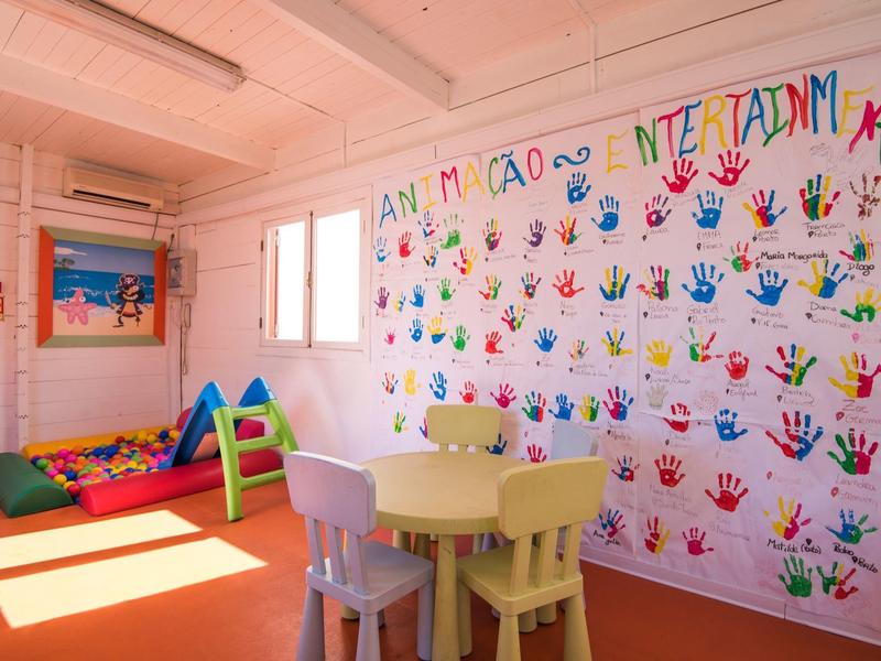 Buntes Kindergartenzimmer mit Handabdruck-Wand, kleiner Sitzgruppe und Spielmatte am Fenster.