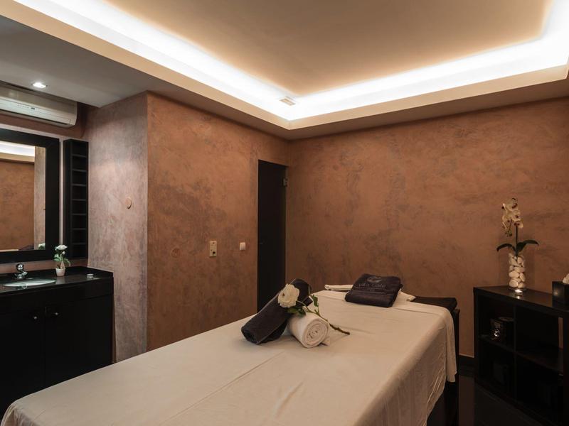 Ruhiger Behandlungsraum mit Massagetisch, braunen Wänden, Deckenlicht und dunklen Möbeln.