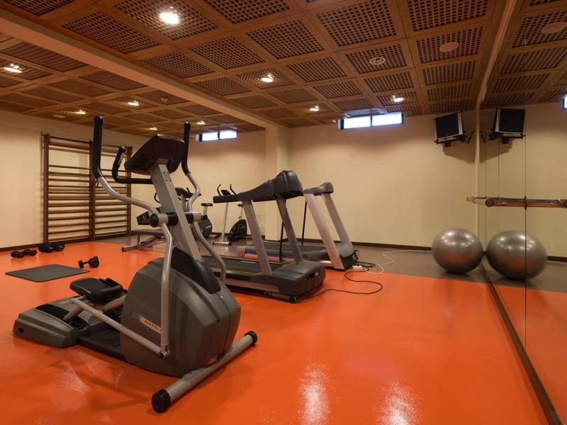 Kleiner Fitnessraum mit orangem Boden, Holzdecke, Laufbändern und Gymnastikbällen an der Wand.