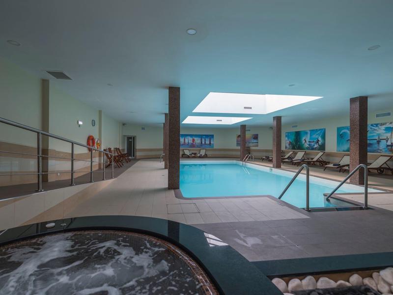 Innen-Schwimmbad mit rechteckigem Pool, Whirlpool im Vordergrund und hellem Oberlicht.