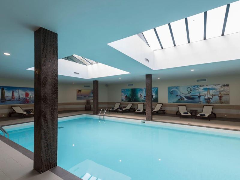 Innenpool mit rechteckigem Becken, blauen Wänden und großem Oberlicht, umgeben von Sitzbereichen.