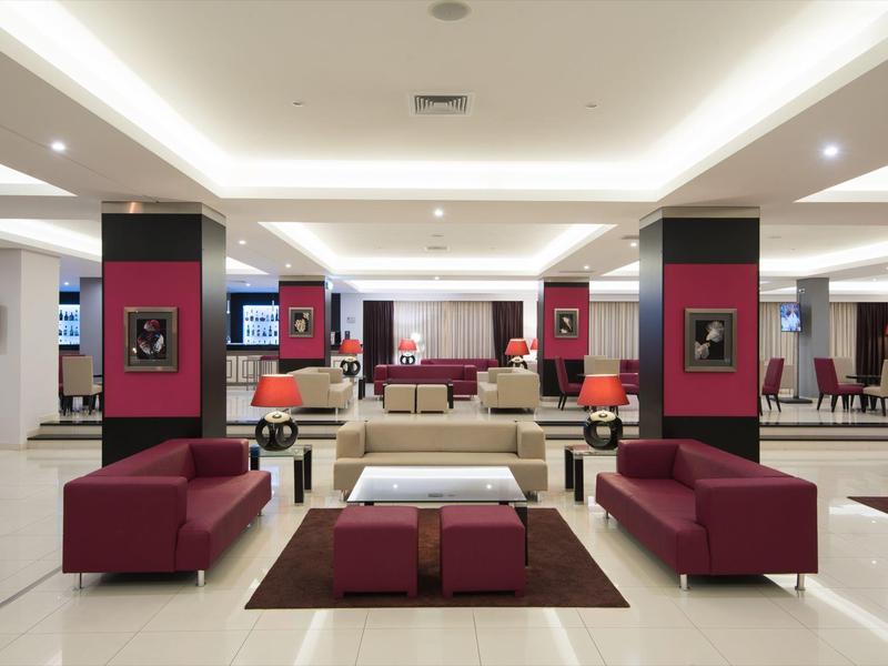 Großer, moderner Hotel-Lobbybereich mit roten Sofas, weißen Tischen und heller Deckenbeleuchtung.