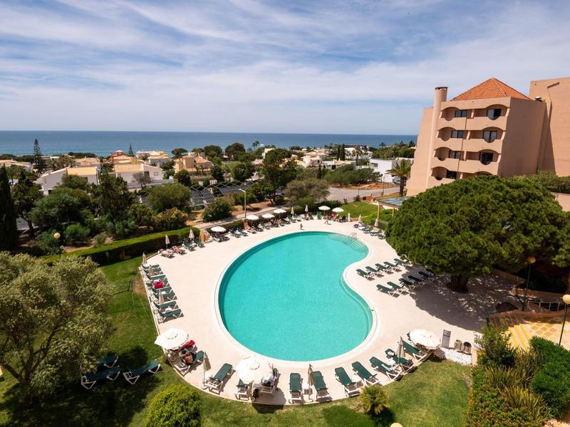 Großer Außenpool mit Liegestühlen, Umgeben von Gebäuden und Blick aufs Meer.