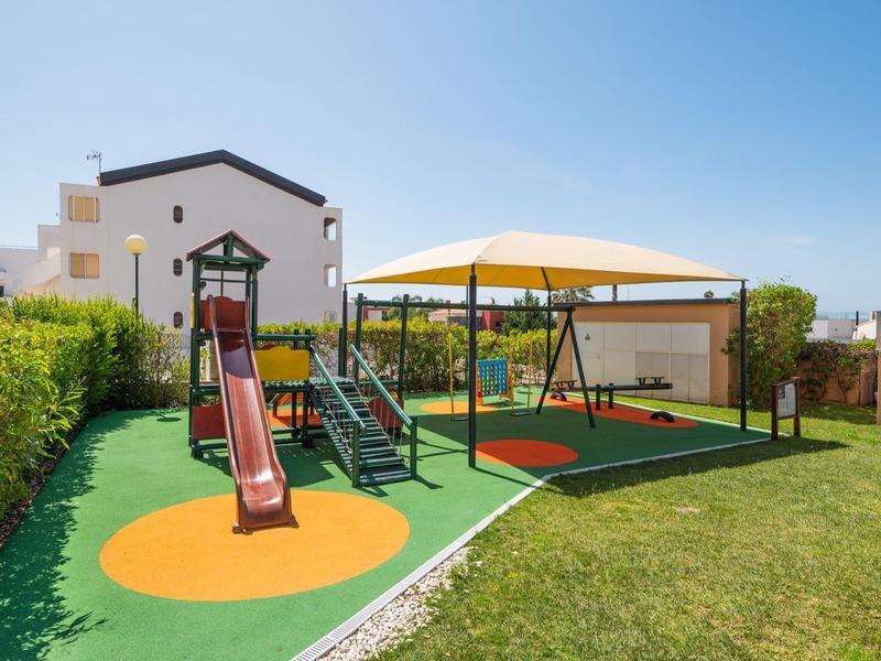Ein moderner Kinderspielplatz mit Rutsche, Kletternetz und Schaukel neben einem weißen Haus.