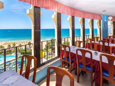 Hotelrestaurant met zeezicht, houten tafels en stoelen naast grote ramen.