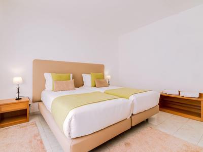 Lichte hotelkamer met twee eenpersoonsbedden, bedlampjes en minimale decoratie.