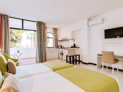 Lichte hotelkamer met twee bedden, bureau, tv en toegang tot een balkon.