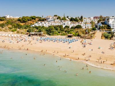 Strand met gouden zand, blauwe zee en hotels op de achtergrond onder een heldere hemel.
