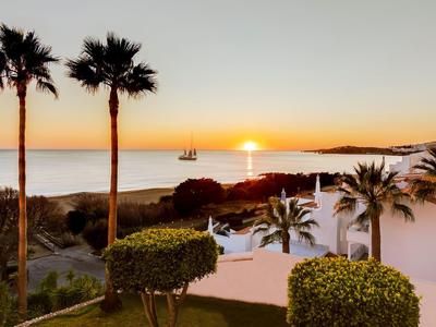 Zonsondergang boven de zee met palmbomen en wit gebouw in tropisch landschap.