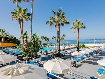 Zwembad met ligbedden en parasols bij palmbomen en zeezicht onder heldere hemel