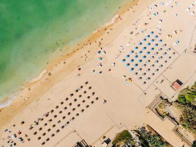 Luchtfoto van een strand met parasols, groen water en aangrenzende gebouwen.