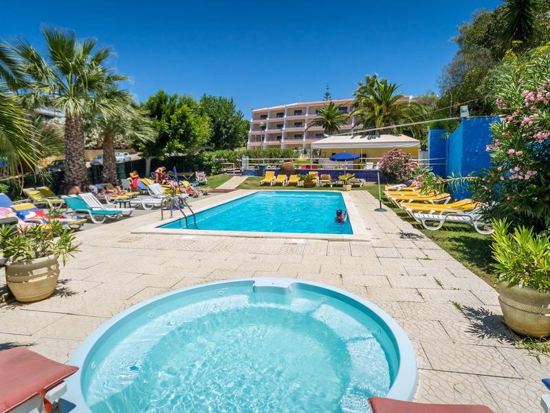 Buitenzwembad en bubbelbad met ligstoelen op zonnige dag bij hotel.