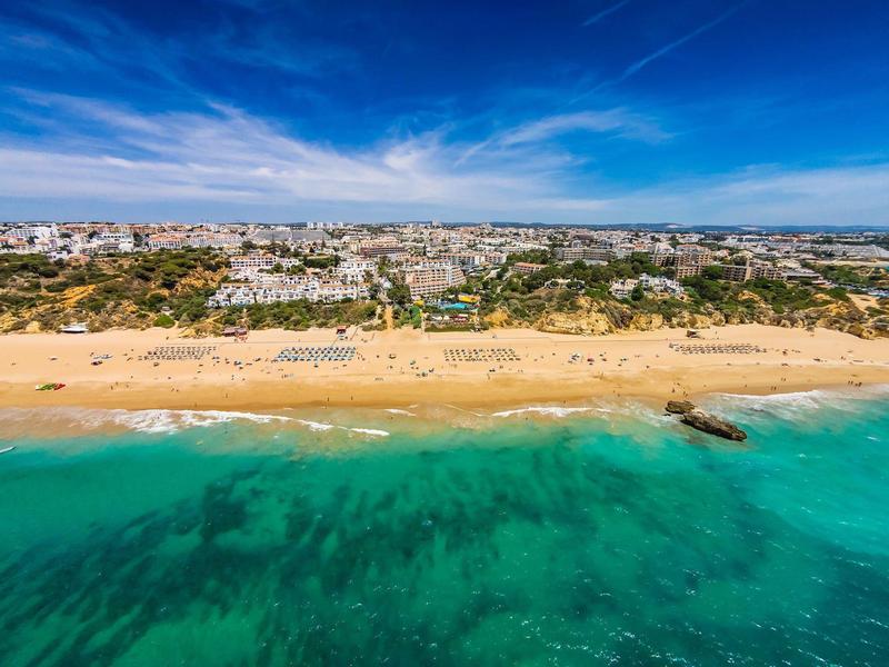 Strand met gouden zand en turquoise zee voor een stad bij zonnig weer.
