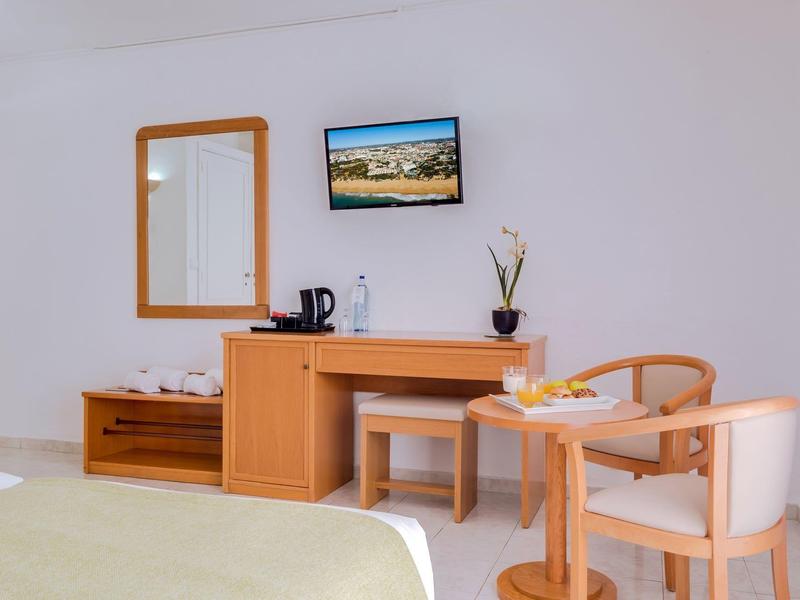 Lichte hotelkamer met houten meubels, tv, spiegel en kleine tafel met stoelen.