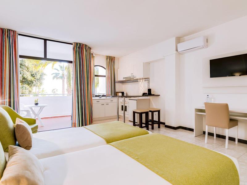 Lichte hotelkamer met twee bedden, bureau, tv en toegang tot een balkon.