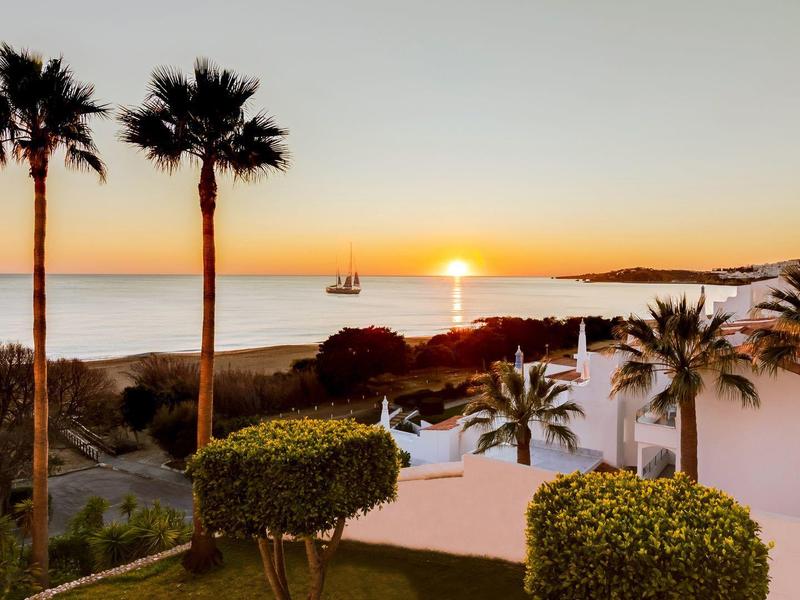 Zonsondergang boven de zee met palmbomen en wit gebouw in tropisch landschap.