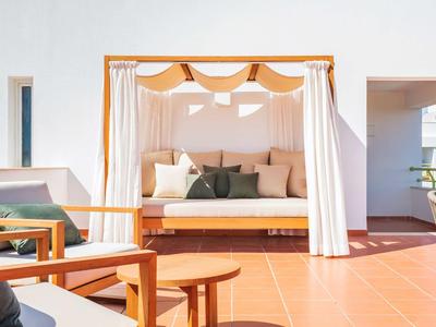 Hell eingerichtete Terrasse mit gemütlichem Tagesbett mit Vorhängen und Holzmöbeln